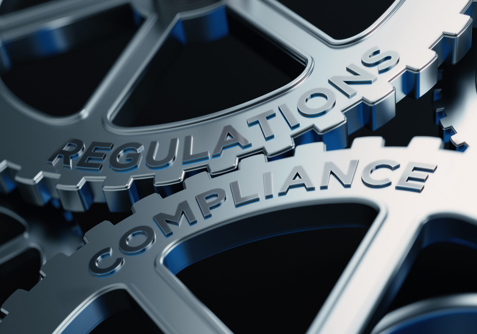 Metal cogs are turning. Regulations and compliance words are written on the cogs. Horizontal composition with copy space.
